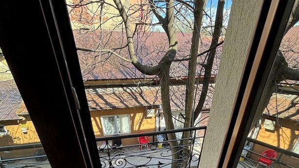 A view from a window to an outdoor balcony with a tiled floor, metal railing, and a red chair. - The Loft Gara de Nord (Bucharest)