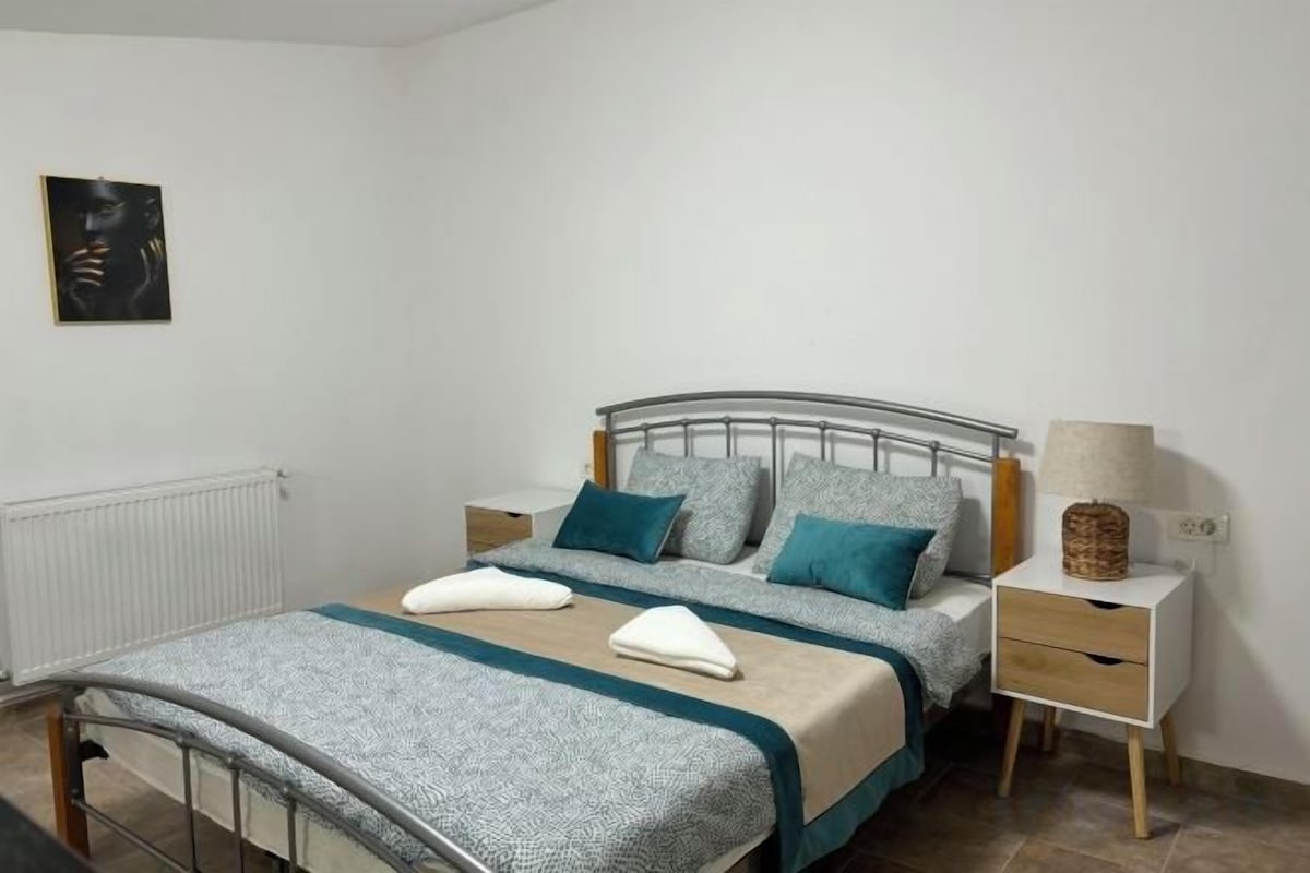 Un dormitorio con una cama de estructura metálica, dos mesitas de noche y un tocador con lámpara.