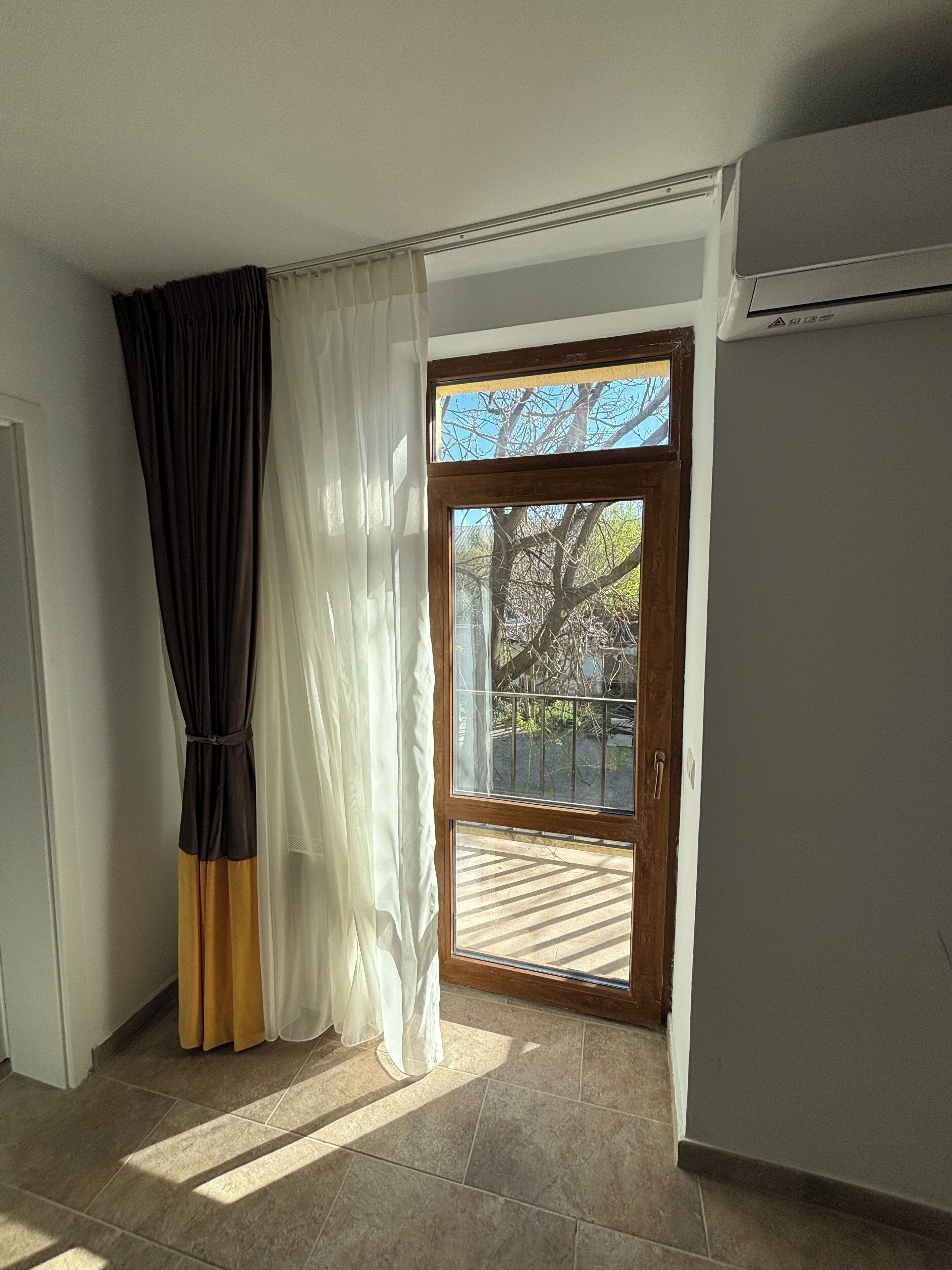Una stanza con una porta scorrevole in vetro che dà su uno spazio esterno, un condizionatore d'aria bianco e un pavimento piastrellato.