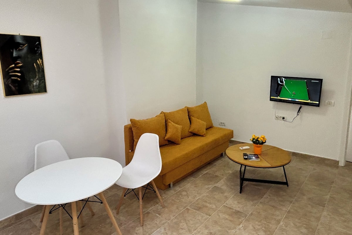 A living room with a sofa, two white chairs, a coffee table, a television, and a painting on the wall.