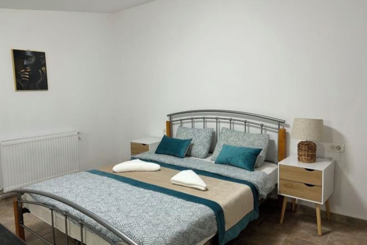 Une chambre à coucher bien rangée, avec un lit à structure métallique, deux tables de chevet et une lampe fixée au mur.