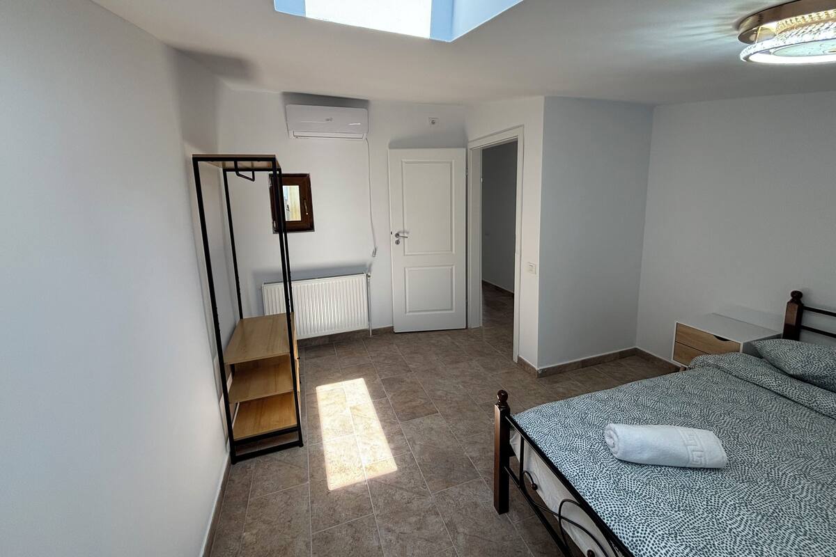 A bedroom with a skylight, a bed with a patterned bedspread, a wooden shelf unit, and a white radiator.