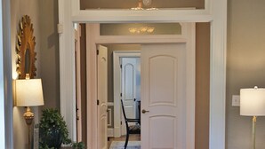 Un salon doté d’un plancher en bois, d’un canapé bleu, d’une console sur laquelle est posée une lampe, et d’une porte qui donne sur une autre pièce.