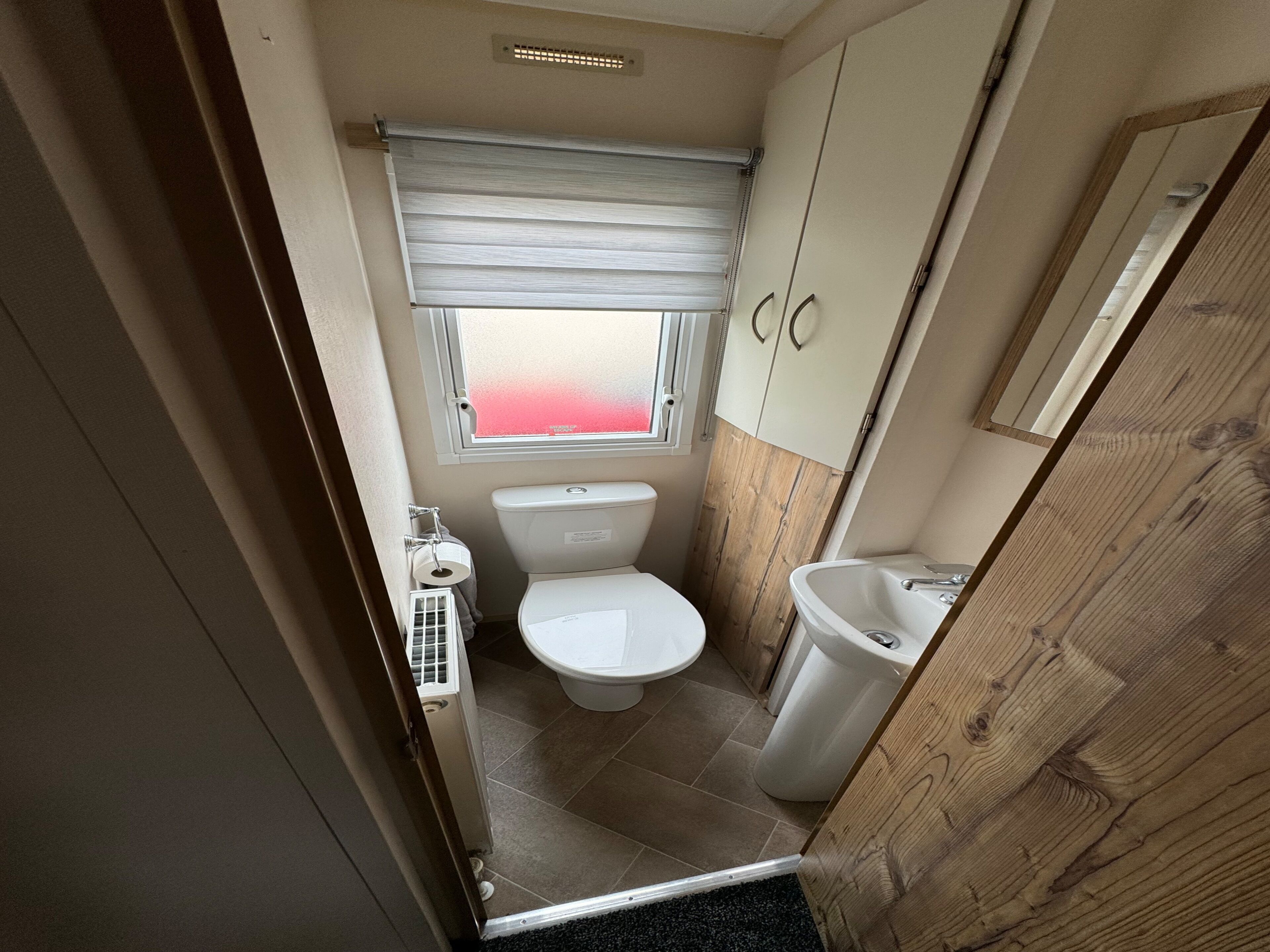 A compact bathroom with a toilet, a sink, and a window with a view.