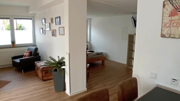 Amplia sala de estar con piso de madera, una mesa de comedor con sillas, un sofá y una mesa de centro. Hay cuadros enmarcados en la pared y una planta en maceta.