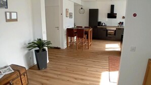 Un amplio salón con piso de madera, una mesa de comedor con sillas, una cocina al fondo y una planta en maceta.