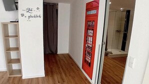Una habitación con suelo de madera, una pared blanca con un cartel que dice 'Zeit glücklich', una cabina telefónica roja y una zona de ducha.