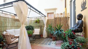 A courtyard with a white sofa, a chair, and a statue of Buddha. There are potted plants and a bamboo fence. - Zen Island downtown Florence, new apartment for 6 (Firenze)