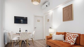 A modern living room with a sofa, a dining table with chairs, a TV, and a door. - Zen Island downtown Florence, new apartment for 6 (Firenze)