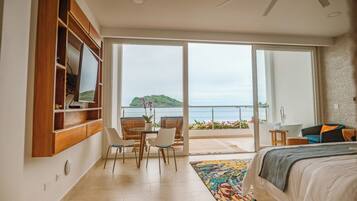 Un dormitorio con una cama grande, un escritorio, sillas, vista al mar y un balcón con bañera.