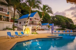 Un complexe hôtelier doté d’une piscine, de chaises longues et d’un bâtiment surmonté d’un toit bleu.