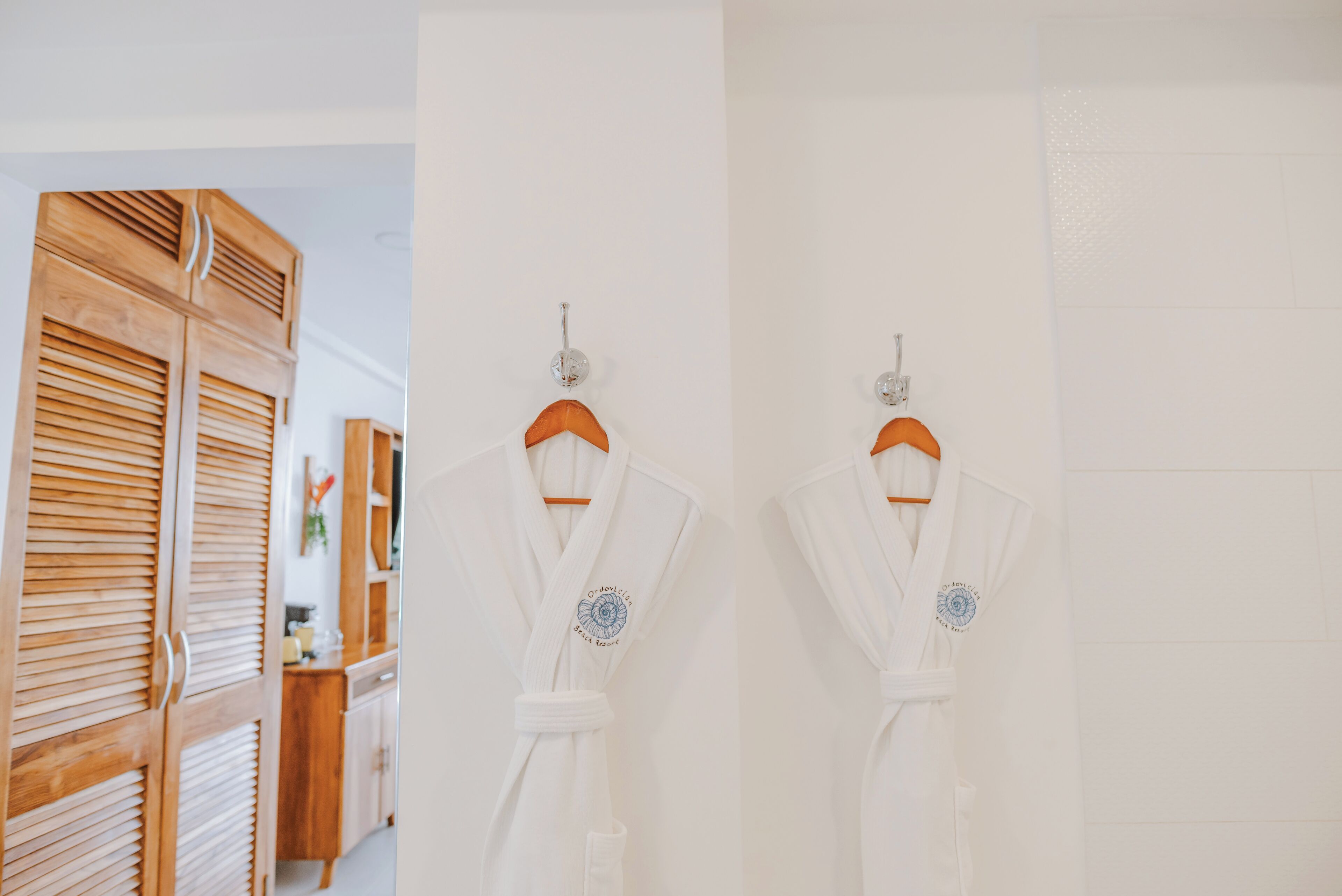 Dos batas blancas colgadas en perchas de madera frente a una pared blanca.