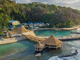 Um resort à beira-mar com bangalôs sobre a água, praia e um píer.