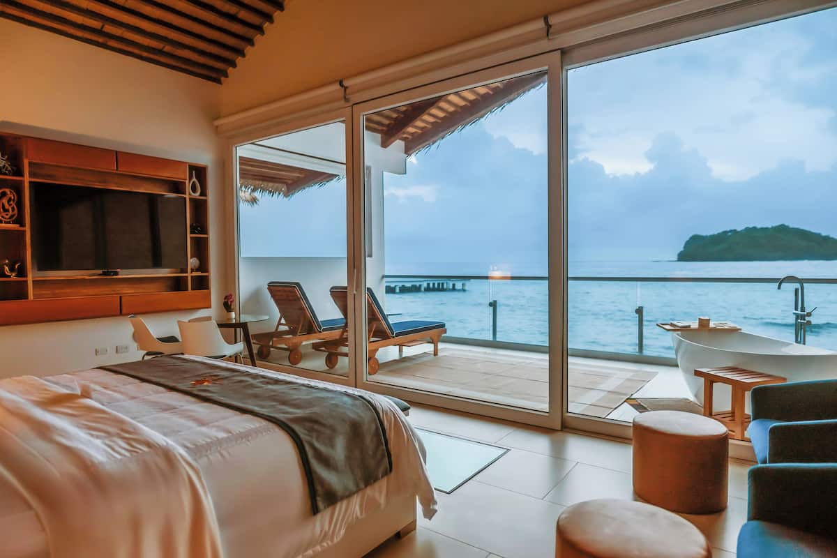 Un dormitorio con cama, televisor y balcón con vista al mar.