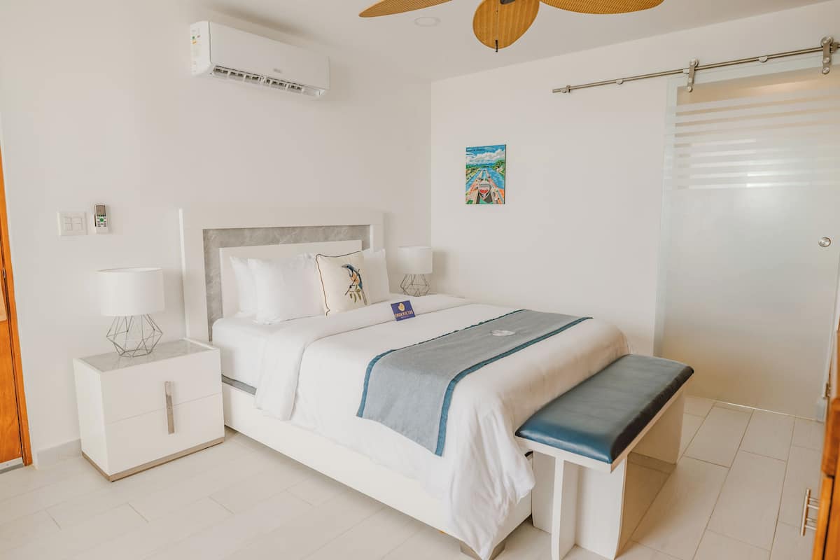 Un dormitorio ordenado con cama, mesitas de noche, un aire acondicionado y un ventilador de techo.