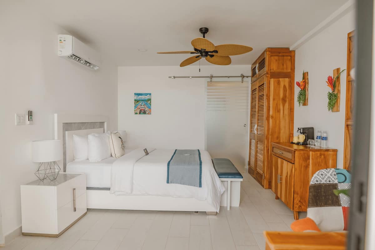 Un dormitorio con cama, mesita de noche, armario de madera, ventilador de techo y aire acondicionado instalado en la pared.