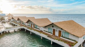 Des bungalows sur pilotis, avec toits de chaume, reliés par un pont, offrant une vue sur des eaux calmes.