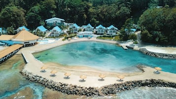 Un complejo turístico con una gran piscina, zona de playa y varios edificios con techos azules.
