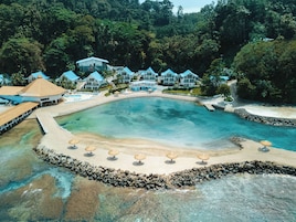 Un complejo turístico con una gran piscina, zona de playa y varios edificios con techos azules.