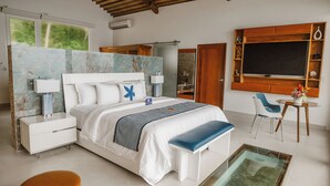 Une chambre moderne avec un grand lit, des tables de chevet, un banc, une table basse en verre et une vue sur l’extérieur.