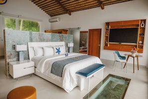 Une chambre moderne avec un grand lit, des tables de chevet, un banc, une table basse en verre et une vue sur l’extérieur.