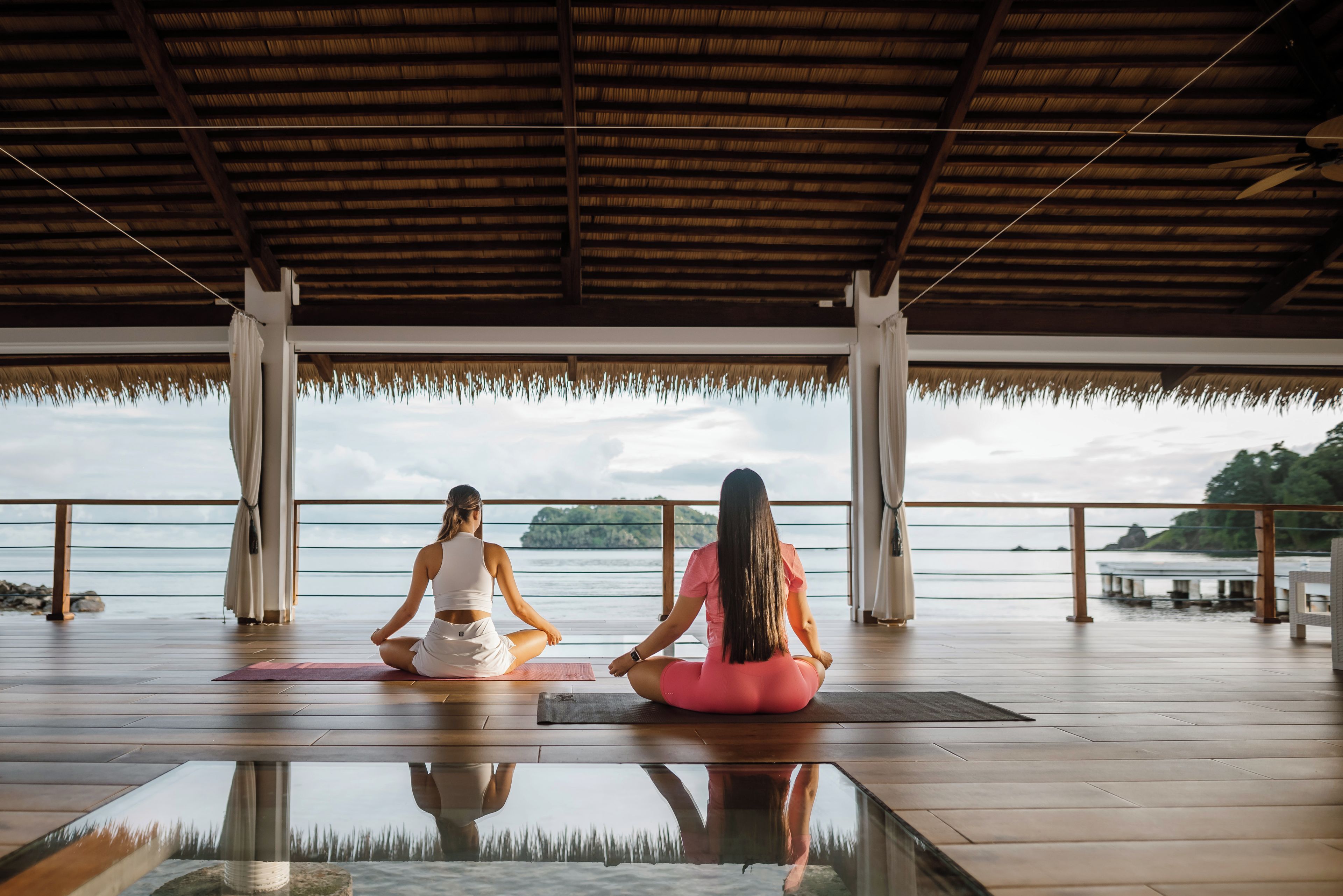 Due persone sedute su tappetini da yoga in una stanza ampia con vista sul mare.