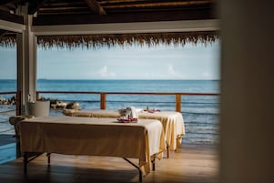 Uma área de spa com duas macas de massagem, um deck de madeira e vista para o oceano.