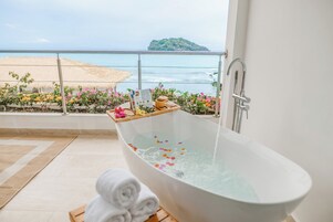 Uma banheira com água, toalhas e flores numa varanda com vista para o mar.