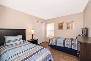 A bedroom with two beds, a nightstand, a lamp, a door, and two framed pictures on the wall. - ⭐NEW LISTING | 4 Bed Villa | Gated Resort of Solana | Pool | Minutes to Disney⭐ (Davenport)
