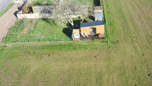 An aerial view of a small, single-story house with a wooden deck, a hot tub, and a fenced garden area.
