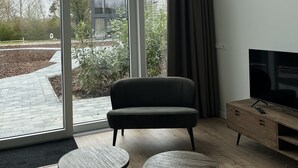 Een moderne woonkamer met een groot raam, een bank, twee kleine tafels en een televisie op een houten dressoir.