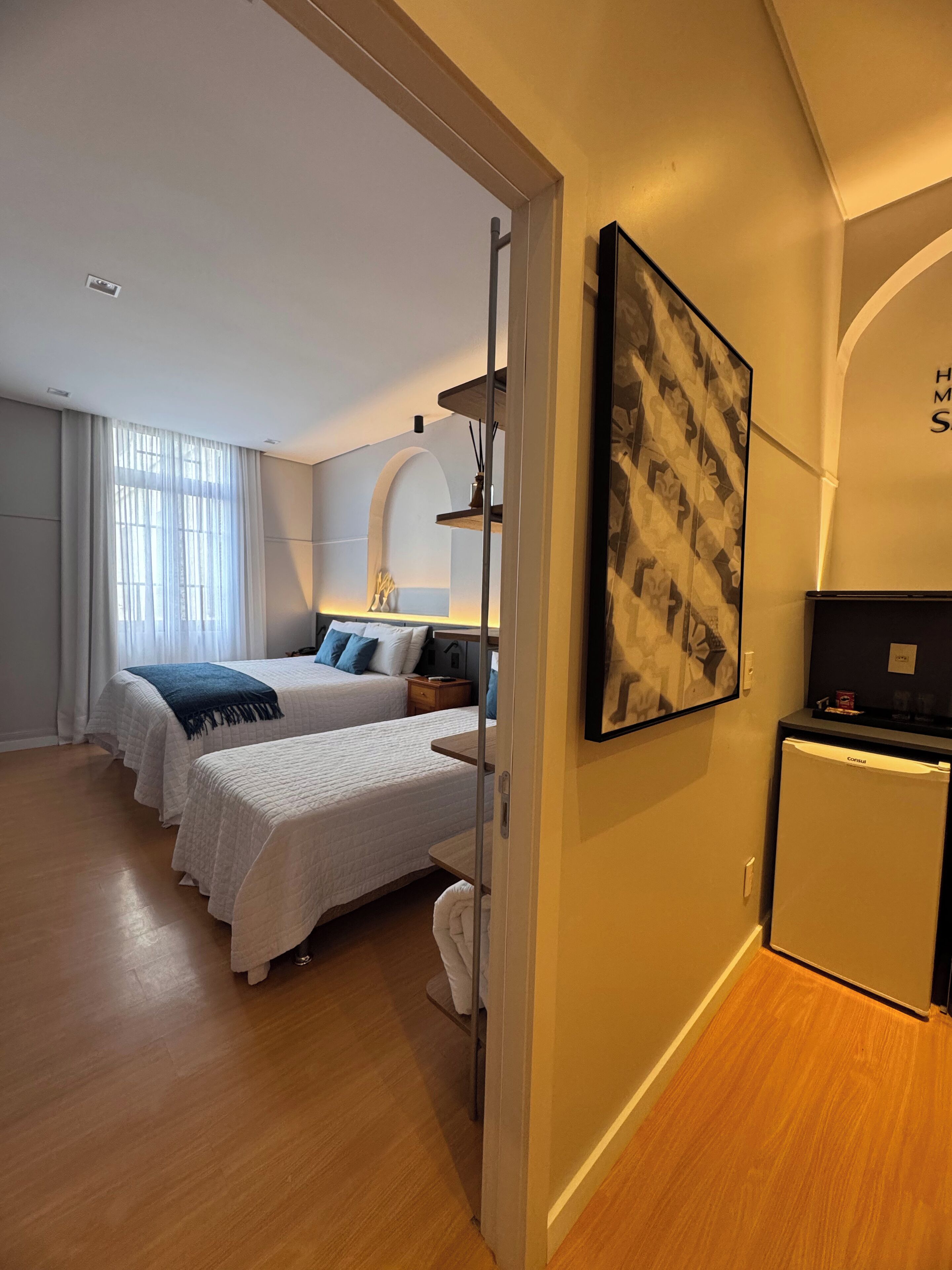 A hotel room with two beds, a small refrigerator, a painting on the wall, and a wooden floor.