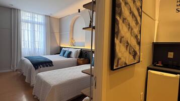 A hotel room with two beds, a small refrigerator, a painting on the wall, and a wooden floor.