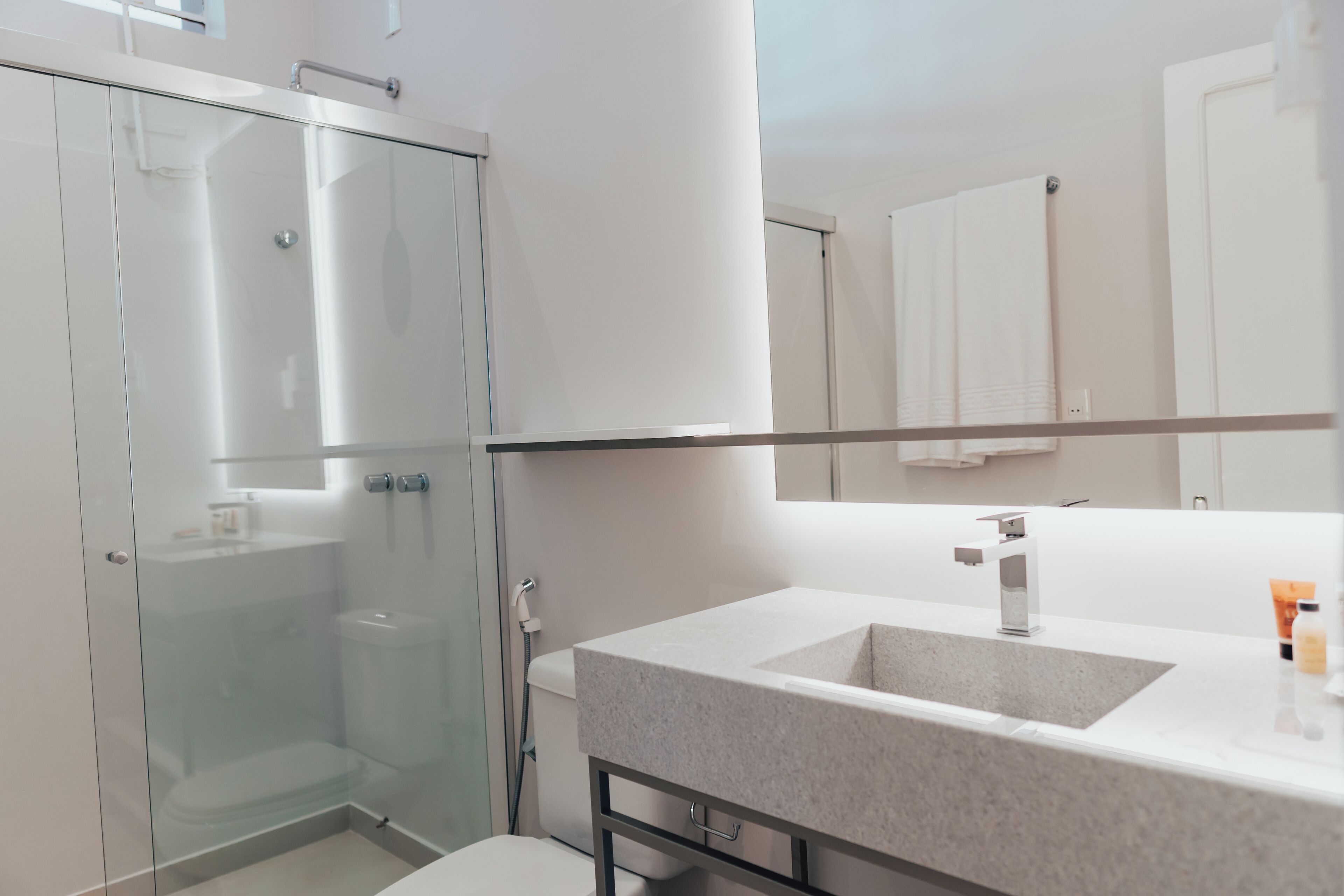 Een moderne badkamer met een douchecabine van glas, een witte wastafel met een marmeren aanrechtblad en een grote spiegel erboven.
