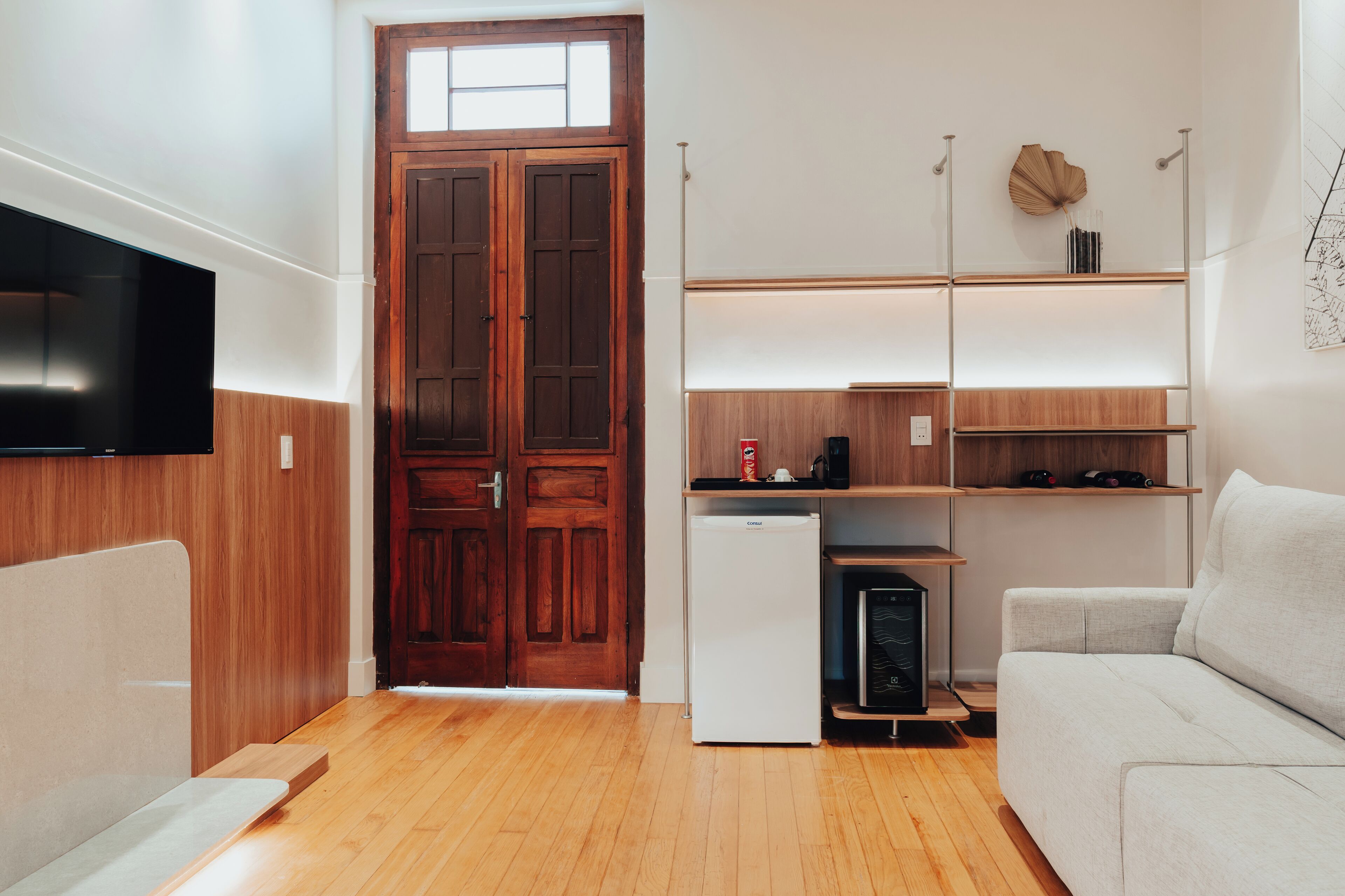 A compact living space with a wooden door, built-in shelving, a white sofa, and a flat-screen TV.