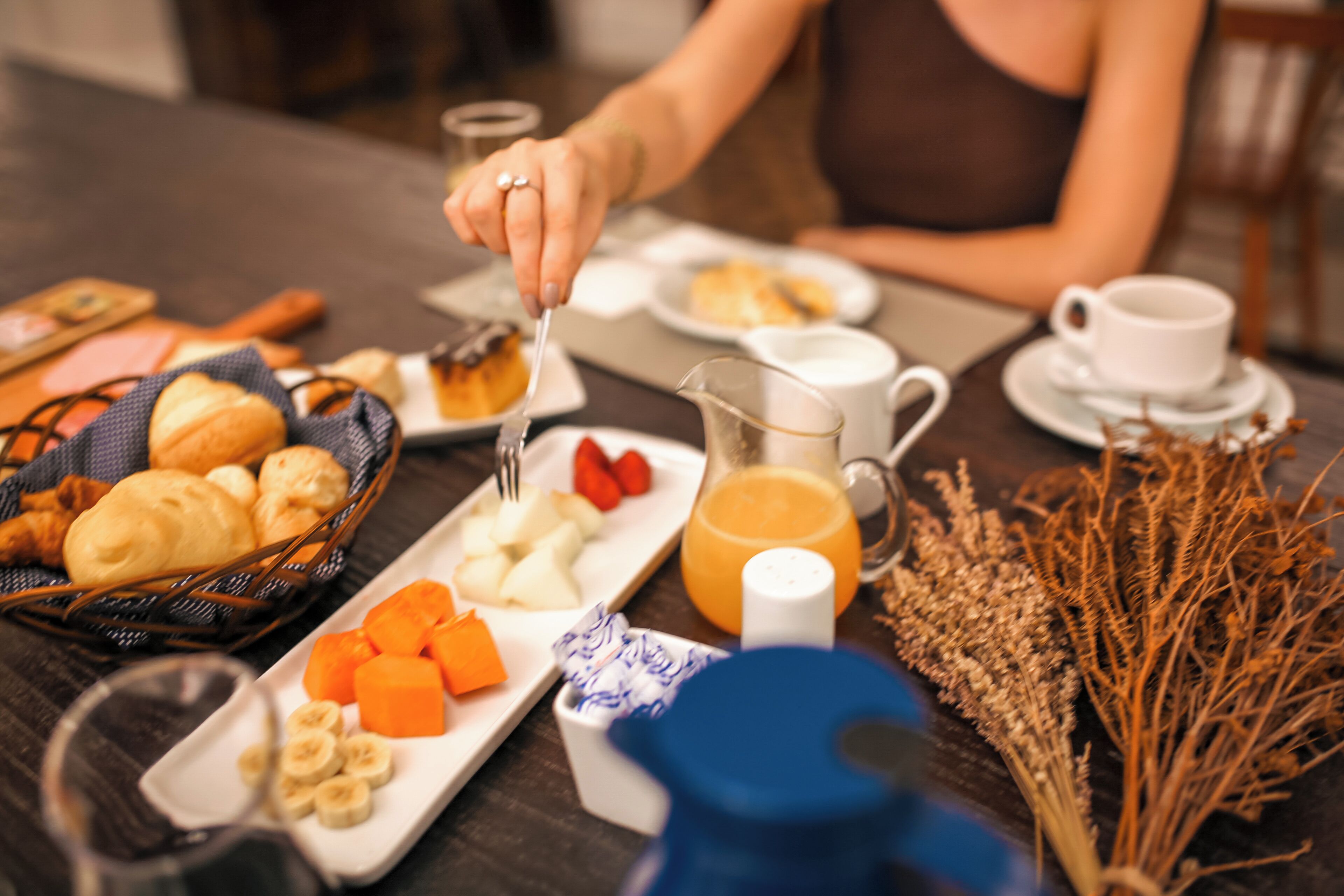A breakfast setting with various food items, a coffee cup, and a jug of orange juice on a table.