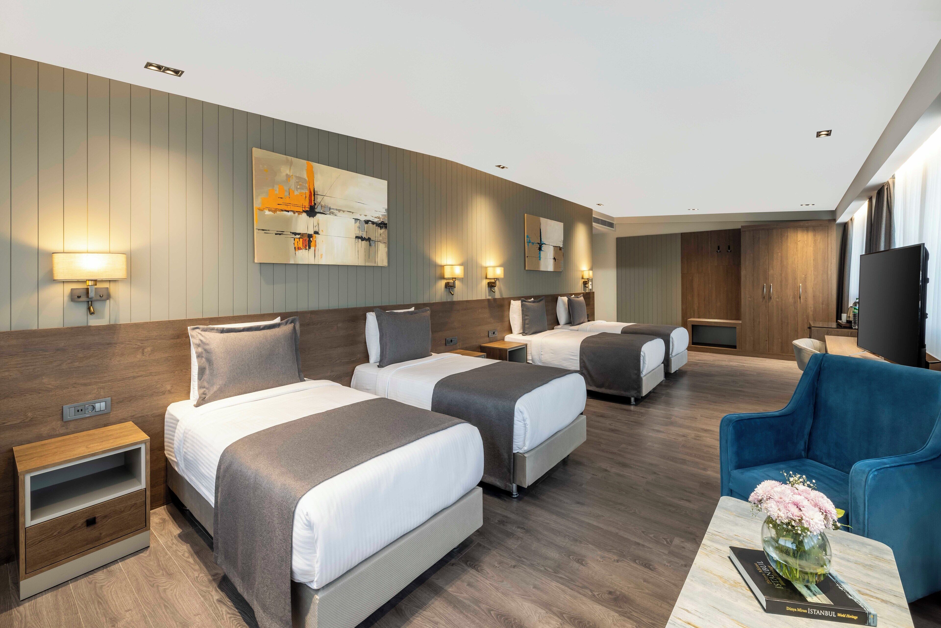 Ett hotellrum med två sängar, en soffa, en tv och en vas med blommor.