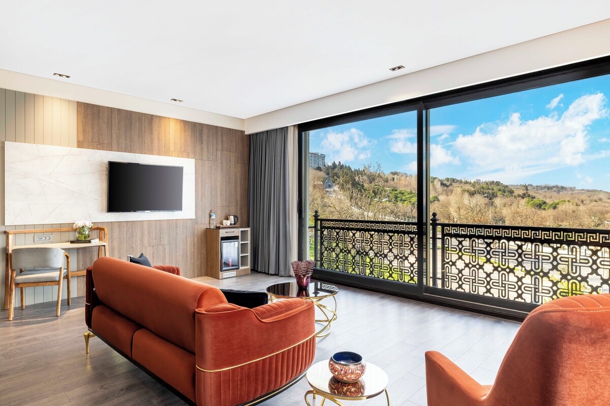 A modern living room with a sofa, a TV, a dining area, and a balcony with a view.