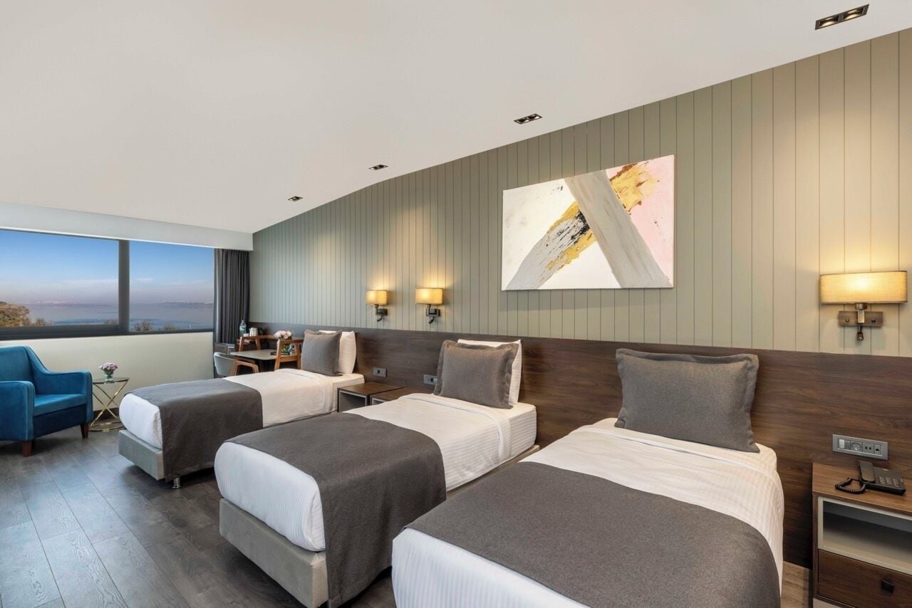 Habitación de hotel con dos camas, un escritorio, una silla y un ventanal con vistas.