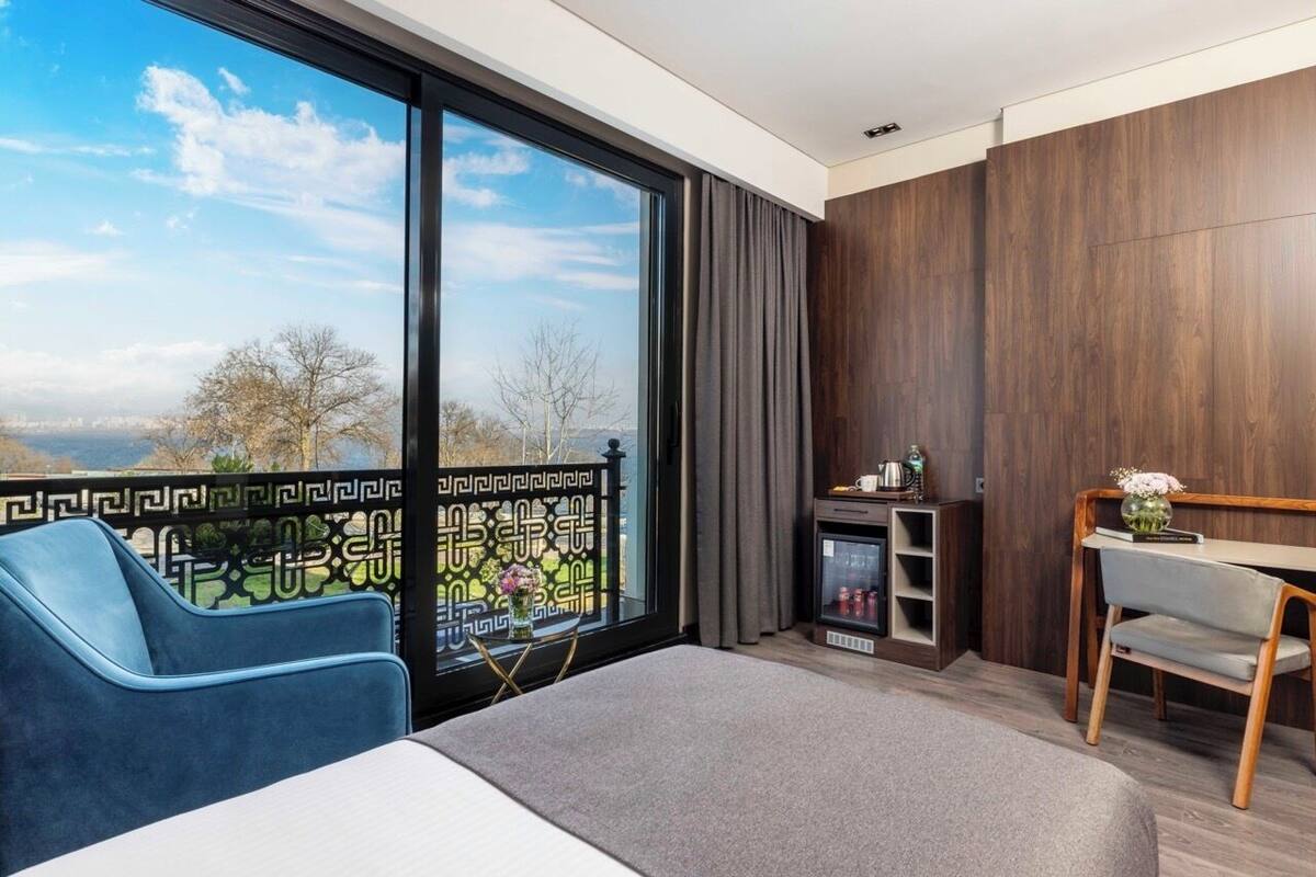 A modern hotel room with a large window, a bed, a desk, and a chair.