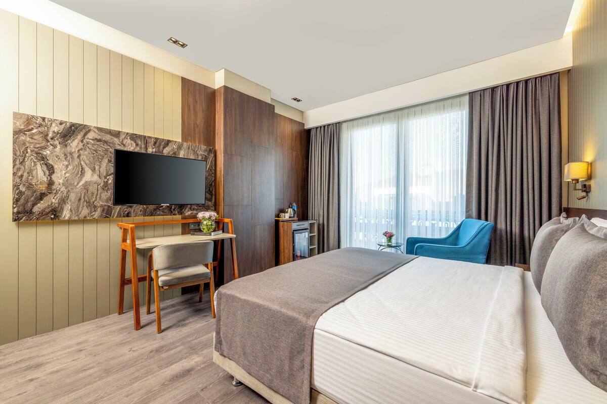A hotel room with a bed, a desk, a chair, a TV, and a window with curtains.