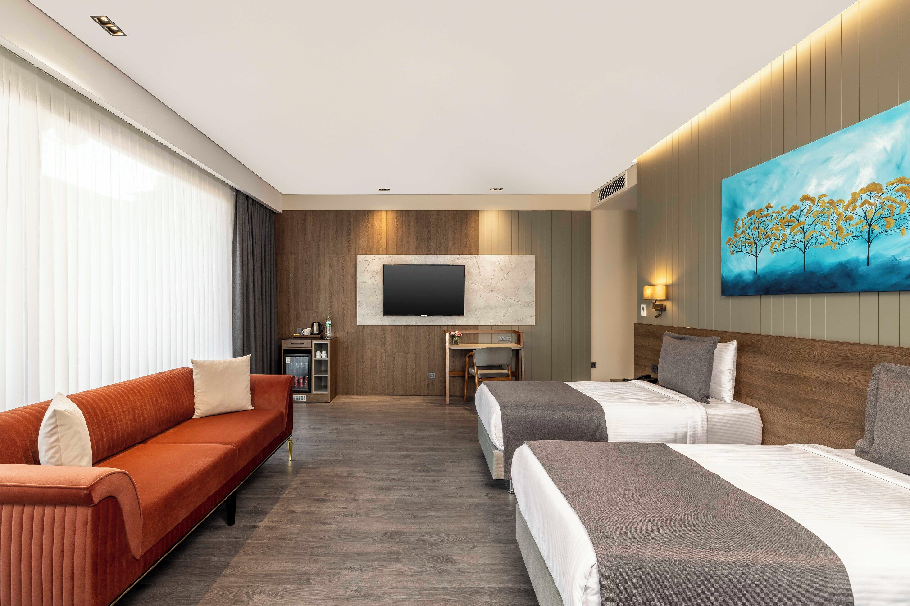 Une chambre d’hôtel avec un canapé, deux lits, une télévision, un bureau et un tableau.