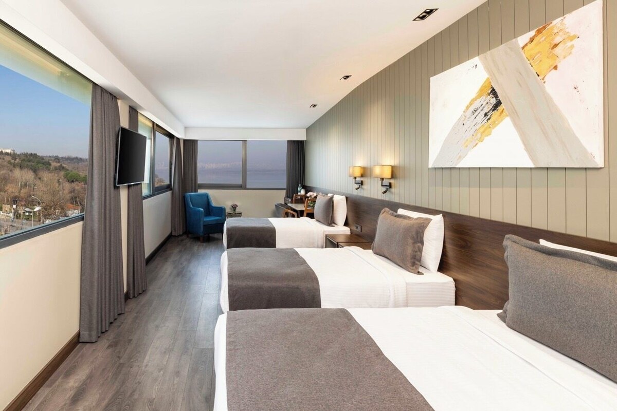 A hotel room with two beds, a TV, a desk, and a view of a cityscape.