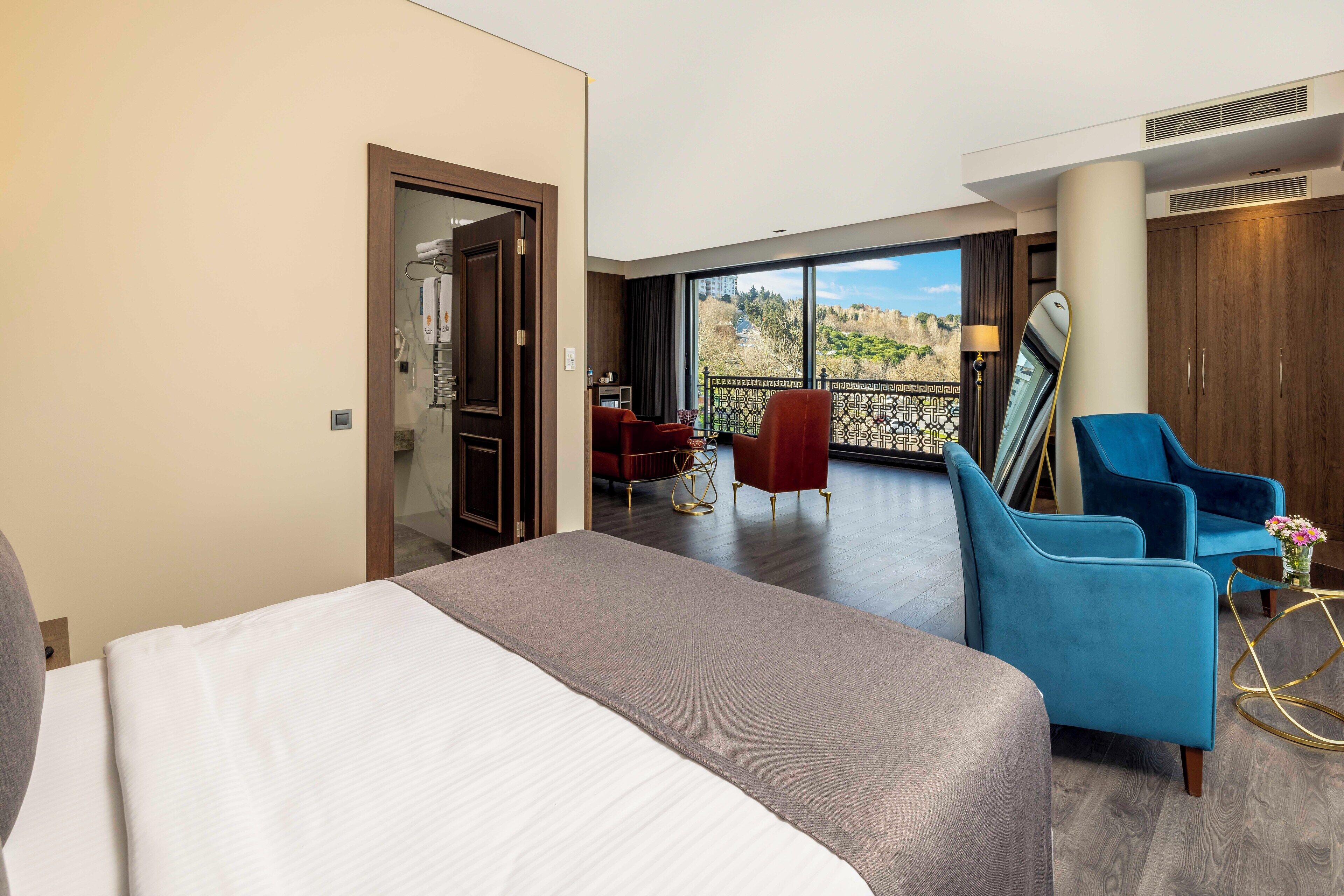 Habitación de hotel con una cama grande, un área de descanso con una silla roja, una silla azul y vistas al exterior.