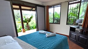 A hotel room with a bed, a desk, and a view of greenery. - Serenity By Nature (Carrillos)