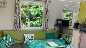 Un salón moderno con un sofá verde, una mesa de vidrio y vistas a la vegetación.