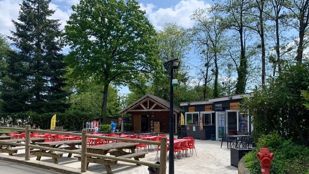 Un área de picnic con bancos de madera y sillas de plástico rojo, una pequeña construcción de madera y un hidrante rojo.