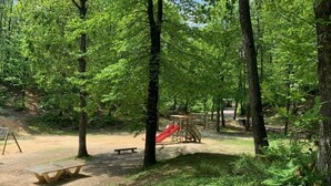 Un parque arbolado con una mesa de picnic, un área de juegos con un tobogán y un banco.