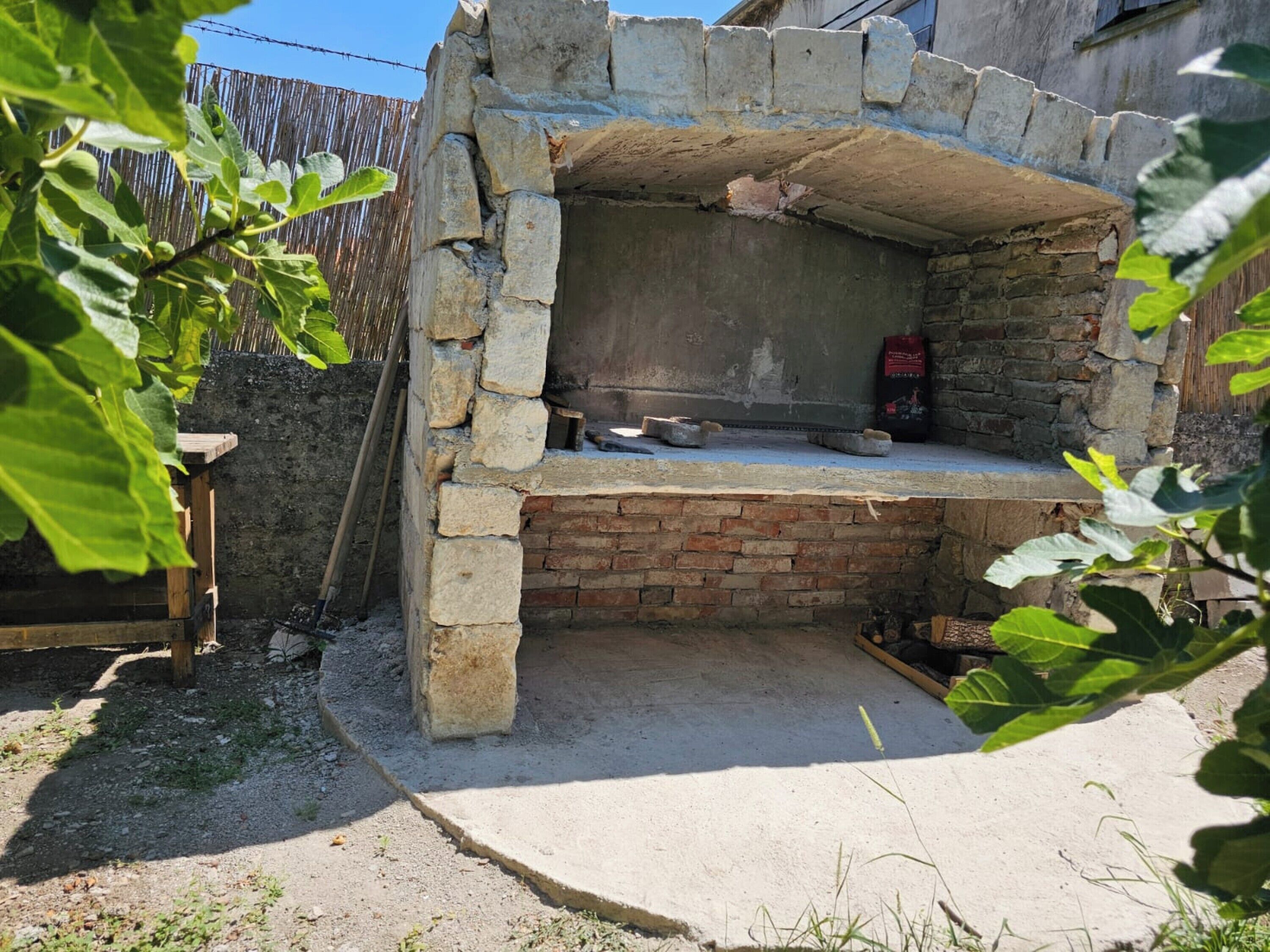 Un four extérieur en pierre, avec une base en briques, entouré d’une zone recouverte de gravier et d’une clôture en bois.