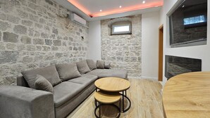 Een moderne woonkamer met een stenen muur, een grijze modulaire bank, een houten salontafel en een open haard.